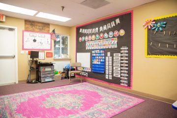 Brightly decorated circle time classroom area with large pink rug and educational materials on the wall